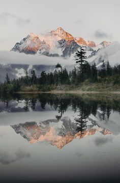 the mountains are covered in clouds and trees as they reflect in the still lake water