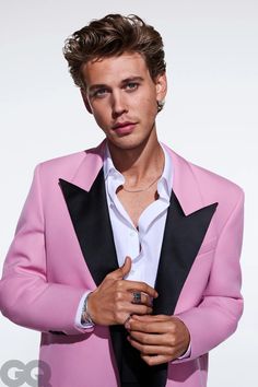 a young man in a pink suit and white shirt is posing for the camera with his hands on his chest