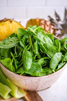 a bowl filled with spinach next to sliced pineapples and other fruit on a table