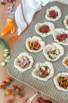 many small pastries are sitting on a baking tray with tomatoes, peppers and cucumbers