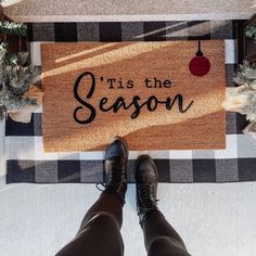 a person standing in front of a door mat that says tis the season