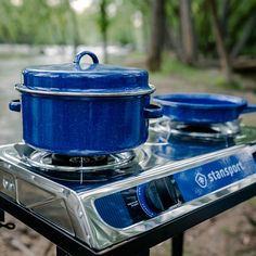 a blue pot sitting on top of a burner oven next to a river with trees in the background