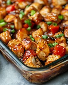 a glass dish filled with chicken, tomatoes and green onions on top of a table