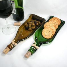 two wine bottles and some crackers on a white table with a glass of wine