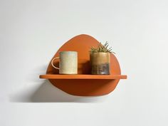 an orange shelf with two mugs and a plant on it