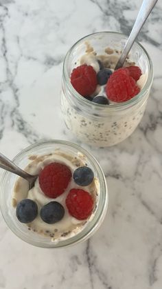 two small jars filled with yogurt and berries on top of a marble counter