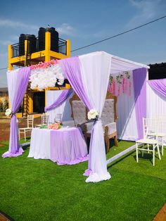 an outdoor wedding setup with purple and white draping on the grass, decorated with flowers