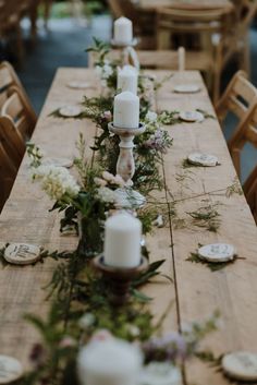 a long wooden table with candles and flowers on it, surrounded by other place settings