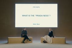 two people sitting on benches in front of a large screen with the words what is the pradaness?