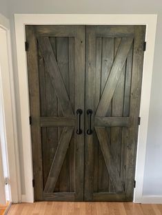 two wooden doors with black handles in a white walled room next to a hardwood floor