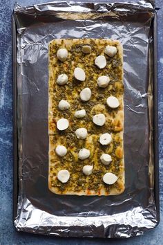 a square pizza covered in cheese and other toppings on top of aluminum foil with a blue background