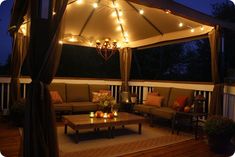 an outdoor living area with couches, tables and lights on the ceiling above it