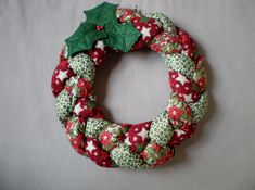 a red and green christmas wreath with holly on it sitting on top of a white sheet