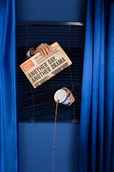 a person pouring something out of a can in front of a window with blue curtains