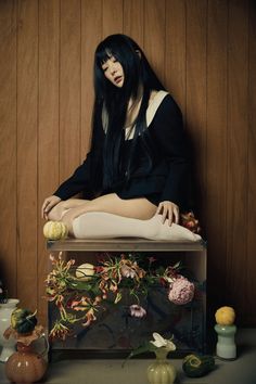 a woman sitting on top of a wooden table next to vases and other items