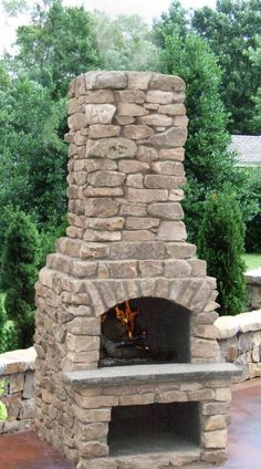 a stone fireplace with a bench in front of it and some trees behind the fire place