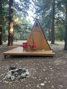 a tent set up in the woods with two red chairs and a fire pit underneath it