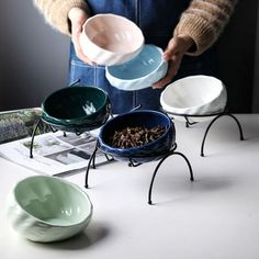 a person is holding three bowls with their hands on the table, while another bowl holds food in it