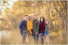 a family posing for a photo in tall grass with trees behind them and yellow leaves on the ground