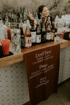 a woman standing behind a counter filled with liquor bottles and glasses on top of it