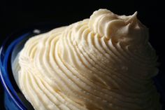 a blue bowl filled with white frosting sitting on top of a table next to a black background