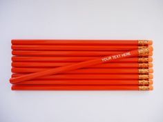 six orange pencils with gold tips are lined up on a white surface and have the words your text here written on them