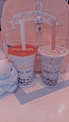 two cups of bubble tea and a teddy bear on a table with a pink purse