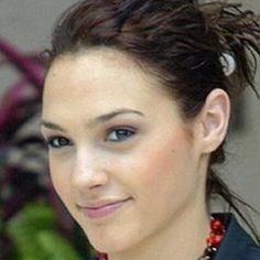 a woman wearing a black jacket and red necklace smiling at the camera with her hair in a bun