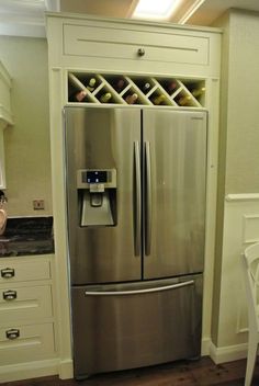 a stainless steel refrigerator in a kitchen next to white cabinets and drawers with wine bottles on the shelves