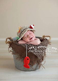 a baby wearing a knitted hat laying in a bucket with a red ornament hanging from it's side