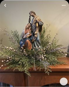 a statue of the virgin mary and child jesus on top of a mantel with greenery