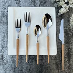 five forks, two spoons and one knife on a white plate with flowers in the background