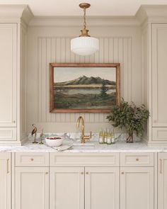 a painting hangs above a kitchen sink with marble countertops and gold faucets