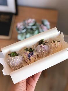 a hand holding a box filled with chocolate covered strawberries