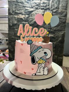 a pink cake decorated with a cartoon character on top and balloons in the shape of a dog