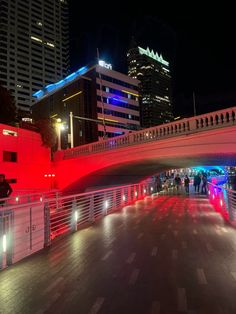 people are walking under an overpass at night with lights on the bridge and buildings in the background