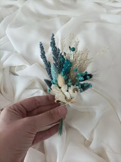 a hand holding a flower on top of a white bed sheet with blue and green flowers