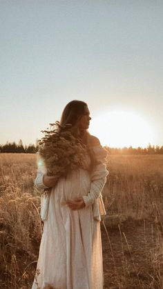 a woman is standing in a field with her hair blowing in the wind and she is wearing a white dress