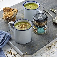 two mugs filled with soup sitting on top of a wooden table next to bread