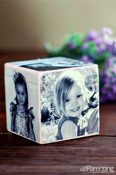 a cube with two pictures on it sitting on a wooden table next to purple flowers