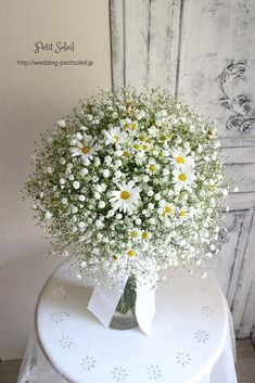 a vase filled with white flowers sitting on top of a small table next to a wall