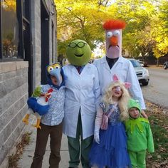 three children and an adult in costume standing next to each other on the sidewalk near a building