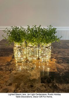 three mason jars filled with greenery sitting on top of a granite counter topped with lights