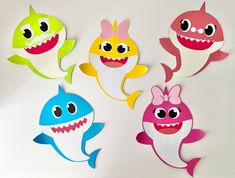 four paper cutouts of different colors and sizes of sharks with big eyes on them