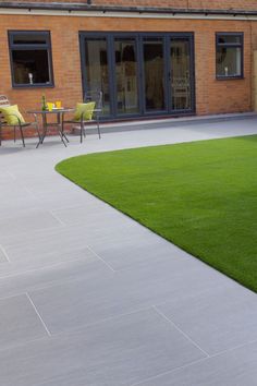 a patio with artificial grass and seating area in the back ground, next to a brick building