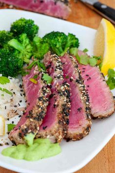 a white plate topped with meat and veggies on top of rice next to lemon wedges