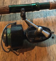 a close up of a fishing reel on a wooden floor with a green handlebar