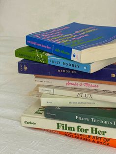 a stack of books sitting on top of a white table cloth covered bedding next to each other