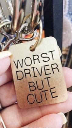 a person holding a keychain that says worst driver but cute