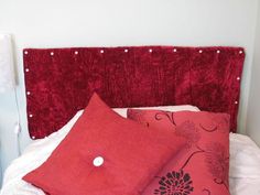 two red pillows sitting on top of a bed next to a white night stand and lamp